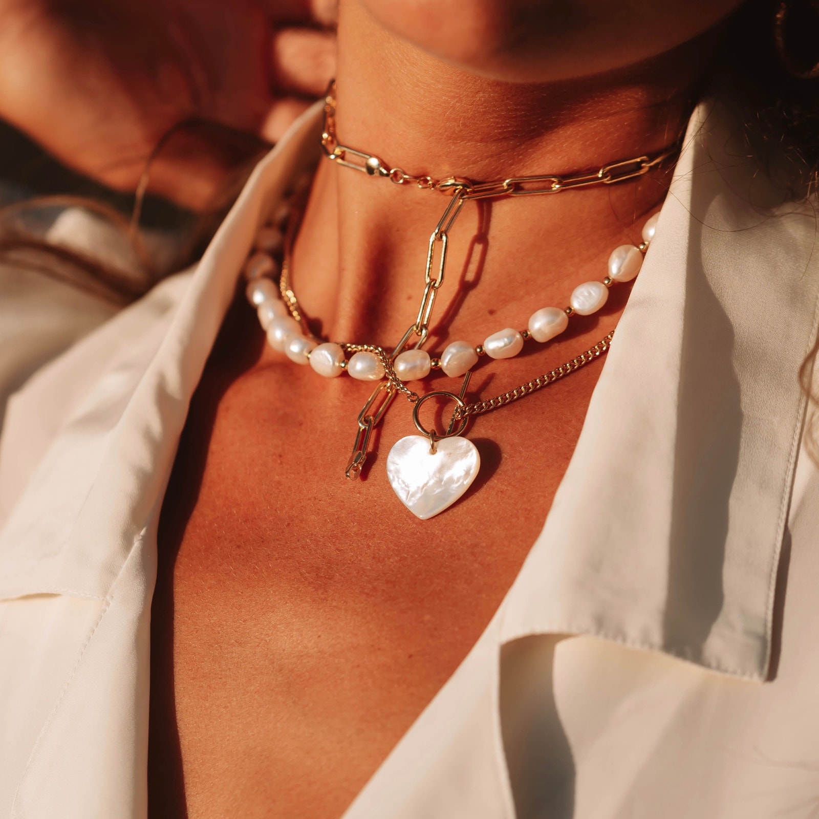 A model in warm sunlight wearing layered gold chains and a pendant.